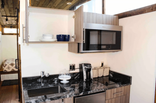 A modern kitchen with dark countertops, a microwave, coffee maker, and open cabinets displaying dishes.